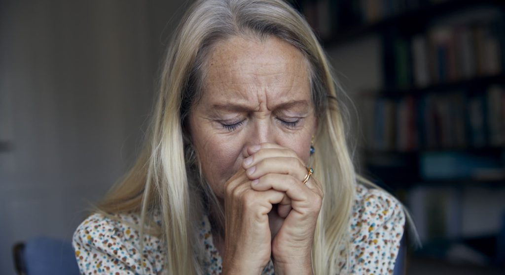Trist kvinde med hænderne foldet op mod ansigtet