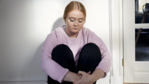 Pige sidder på gulvet og ser nedtrykt ud